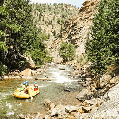 a yellow raft floats through the lower clear creek canyon with trees and cliffs on the left and right sides