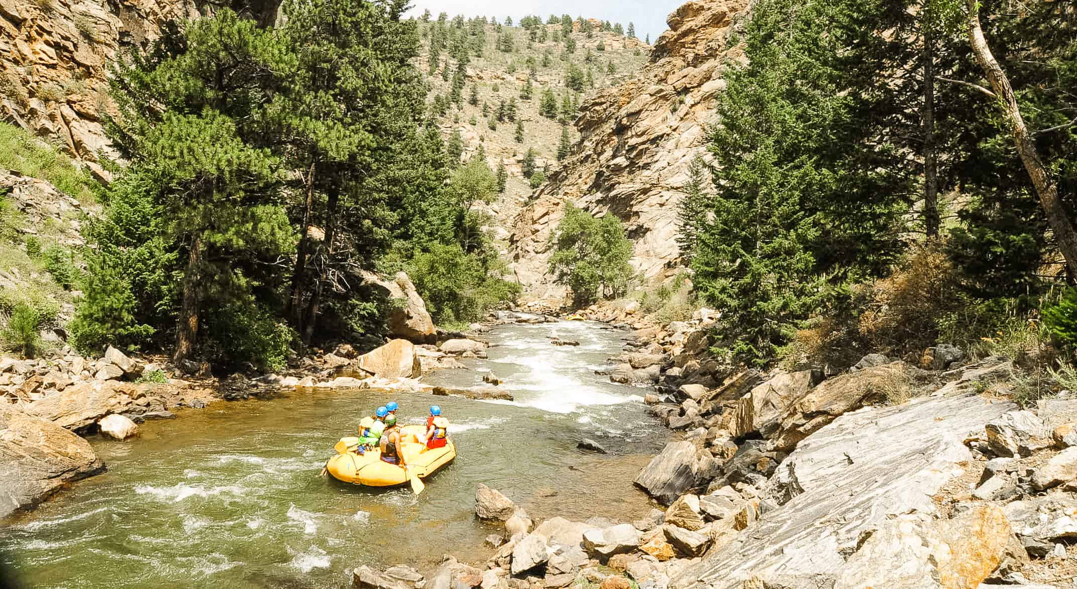 a yellow raft floats through the lower clear creek canyon with trees and cliffs on the left and right sides