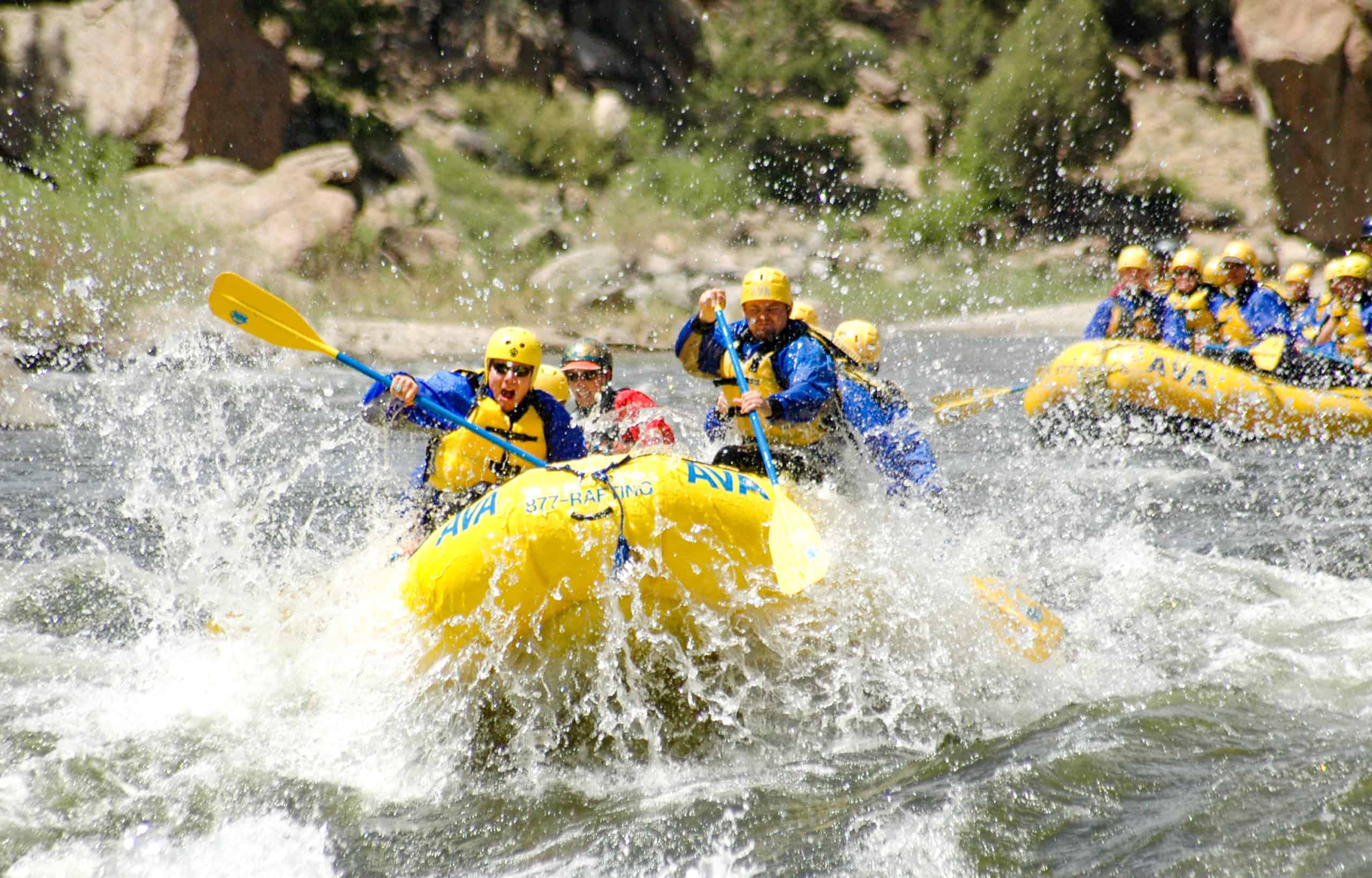 A group of rafters splash into whitewater while another raft follows closely behind