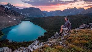 man sitting above alpine lake